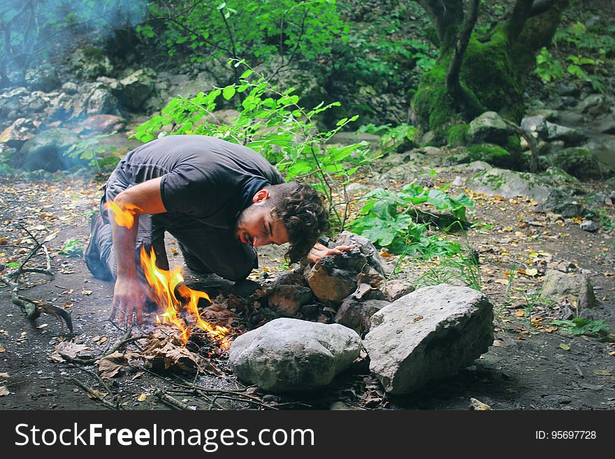 Camping man making fire in countryside, breathing on flames.