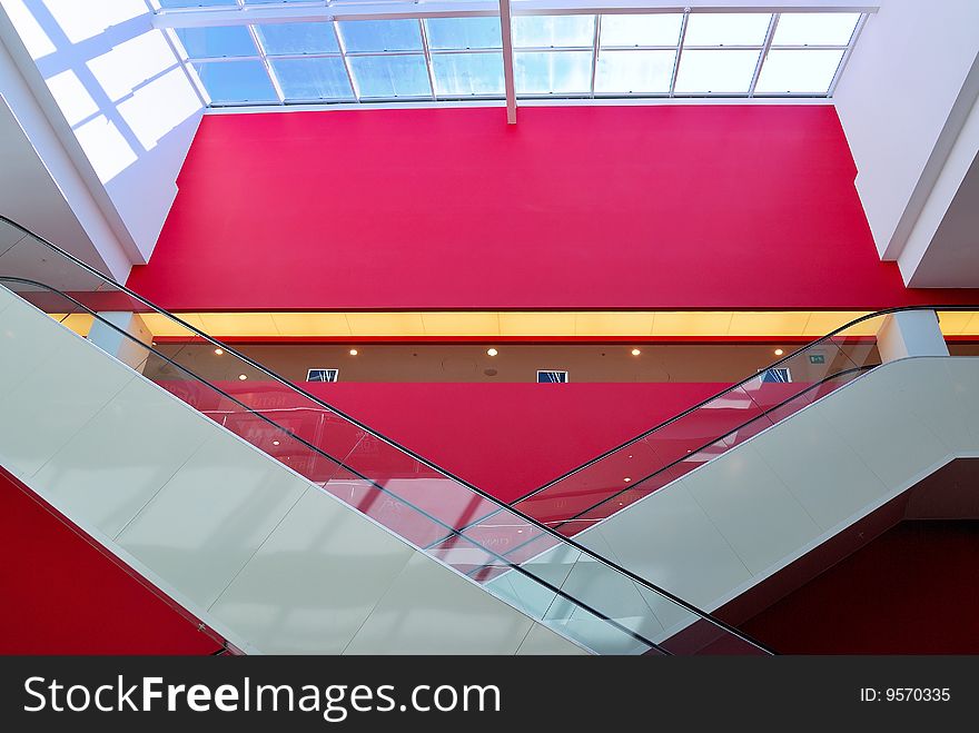 Pair of rolling stairs with red wall in background and glass roof above