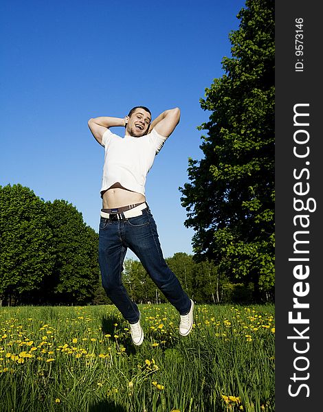 The beautiful young man in park jumps in the sky. Laughs, hands behind a head. In a vest white, jeans and gym shoes. The beautiful young man in park jumps in the sky. Laughs, hands behind a head. In a vest white, jeans and gym shoes