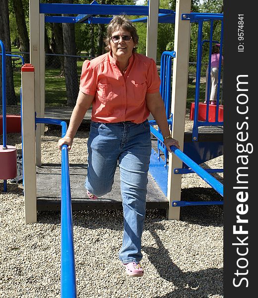 This mature lady is being active at a playground with the parallel bars. This mature lady is being active at a playground with the parallel bars.