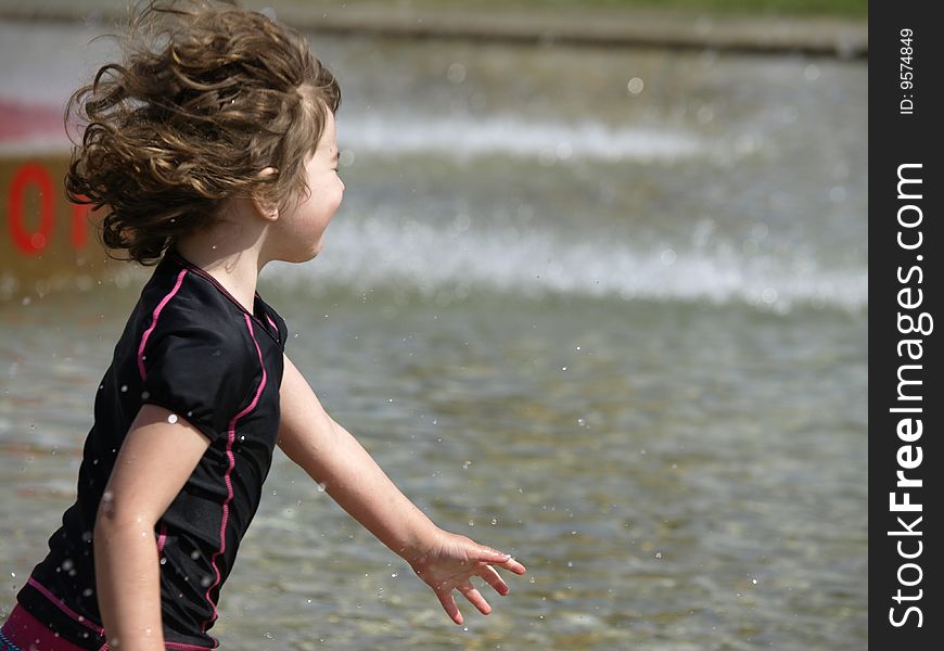 This young girl was having fun running through water at a spray park. This young girl was having fun running through water at a spray park.