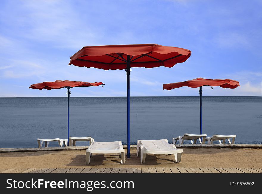 Image of red parasols and white sunbeds on a beach. Image of red parasols and white sunbeds on a beach