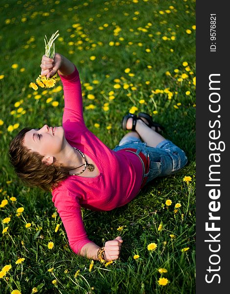 A young cheerful woman having fun on a dandelions glade