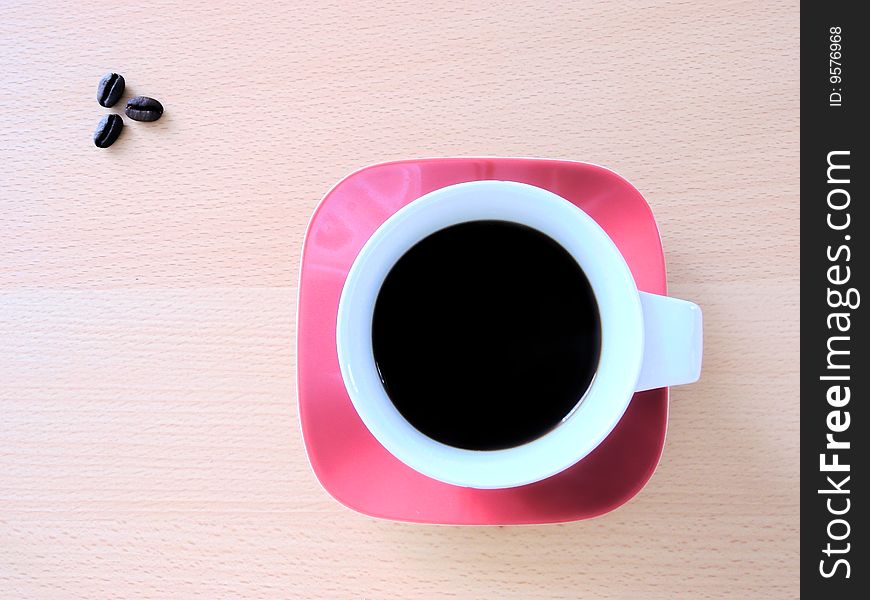 Cup of strong and black coffee on a red squared saucer, in the left upper corner 3 coffee grains.