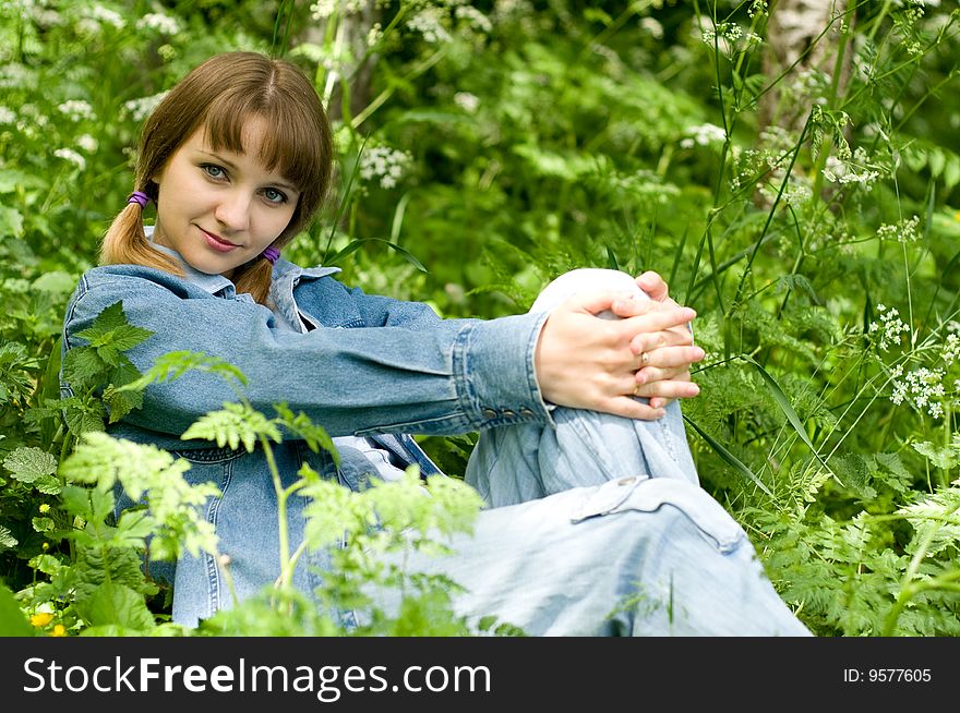 The beautiful girl in park sits on a green grass