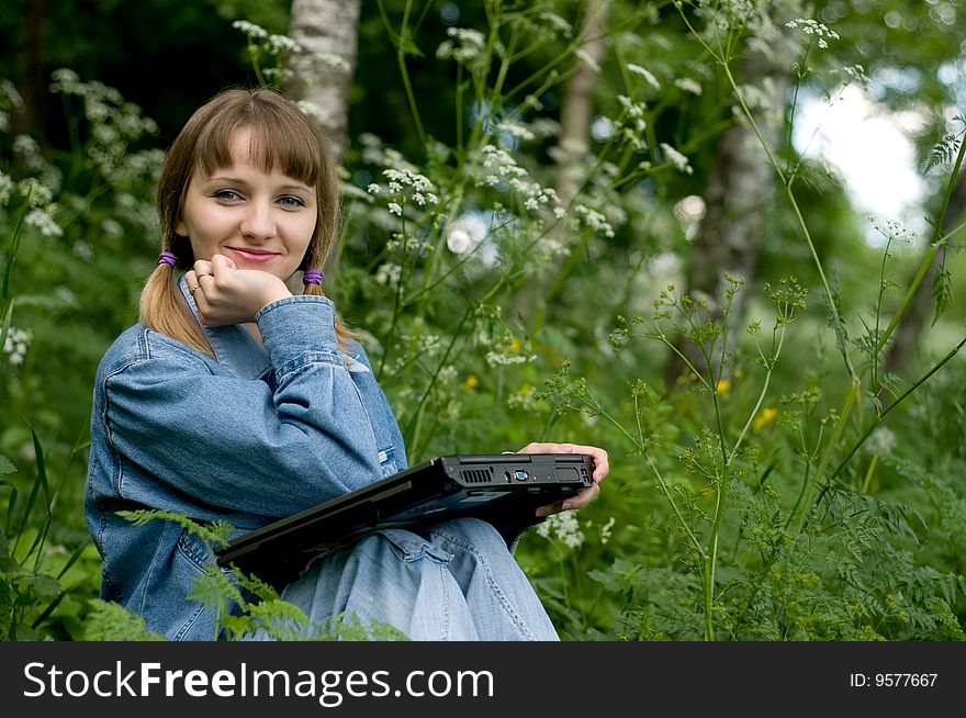 The beautiful girl with the laptop in park sits in a green grass. The beautiful girl with the laptop in park sits in a green grass