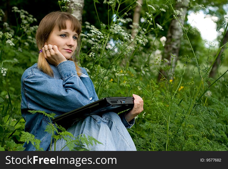 The beautiful girl with the laptop in park sits in a green grass. The beautiful girl with the laptop in park sits in a green grass