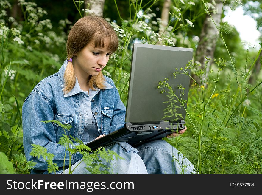 The beautiful girl with the laptop in park sits in a green grass. The beautiful girl with the laptop in park sits in a green grass