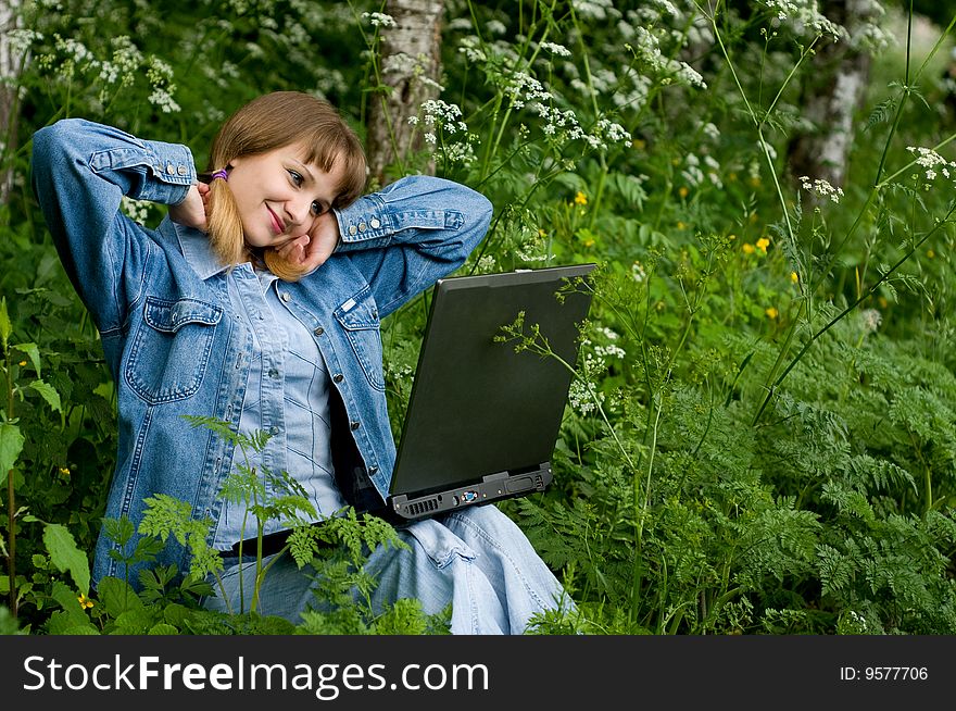 The beautiful girl with the laptop in park sits in a green grass. The beautiful girl with the laptop in park sits in a green grass