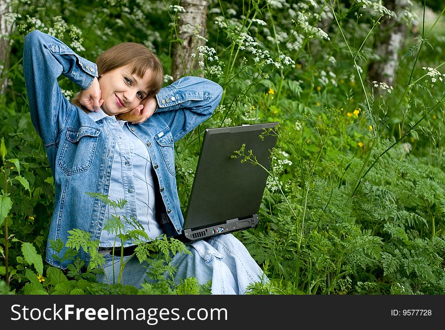 The beautiful girl with the laptop in park sits in a green grass. The beautiful girl with the laptop in park sits in a green grass