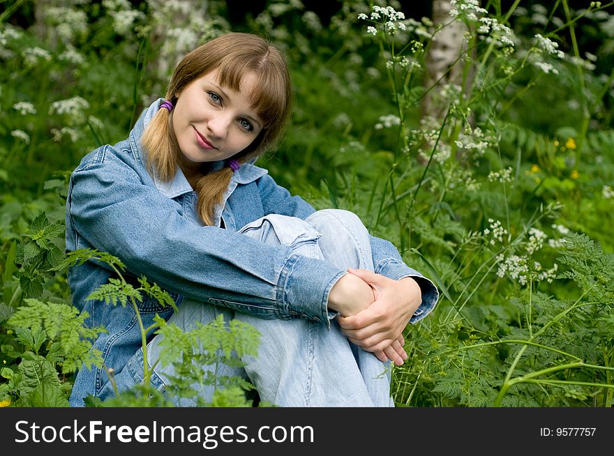 The beautiful girl in park sits on a green grass