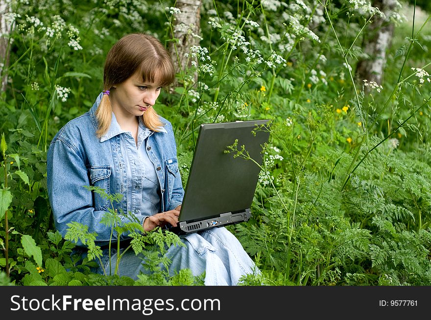 The beautiful girl with the laptop in park sits in a green grass. The beautiful girl with the laptop in park sits in a green grass