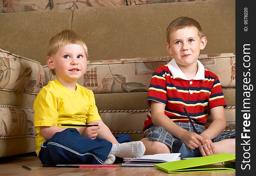 Two boys draw with paints sitting on floor