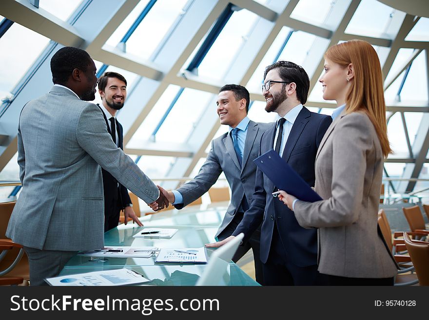 Business professionals shaking hands standing around conference room table.