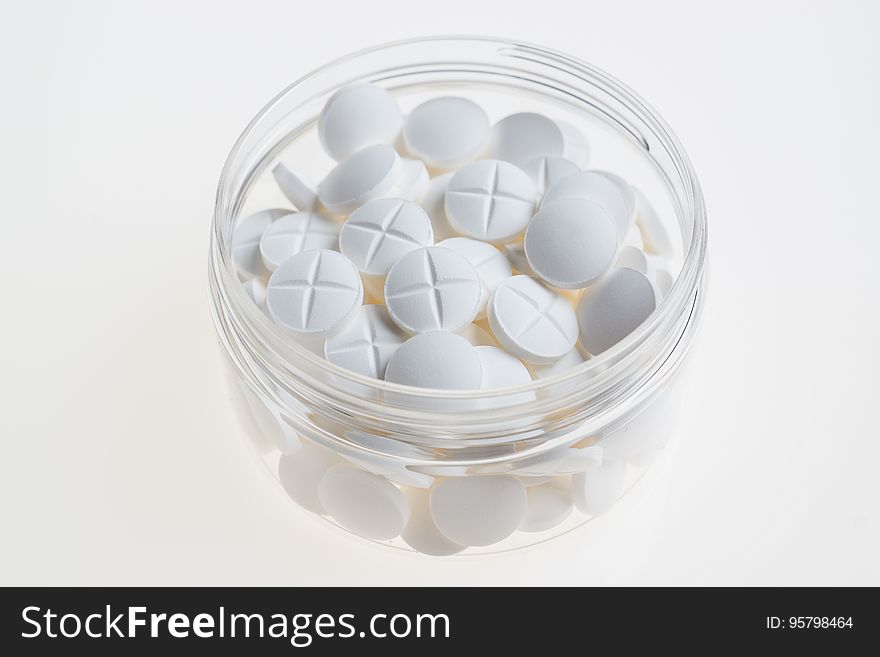 A transparent cup with white pills. A transparent cup with white pills.