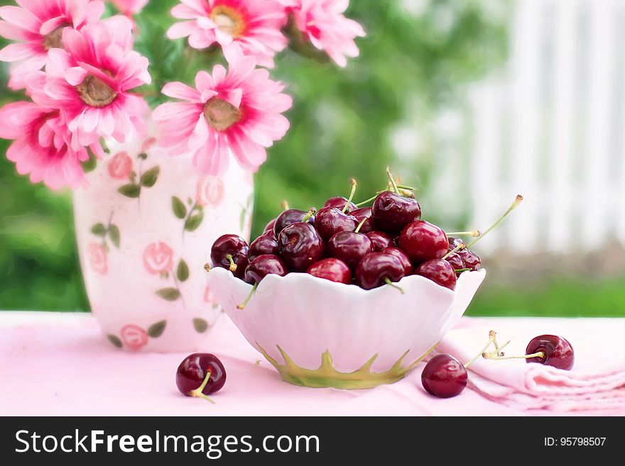 Bowl of fresh ripe whole red cherries next to china vase with pink flowers. Bowl of fresh ripe whole red cherries next to china vase with pink flowers.