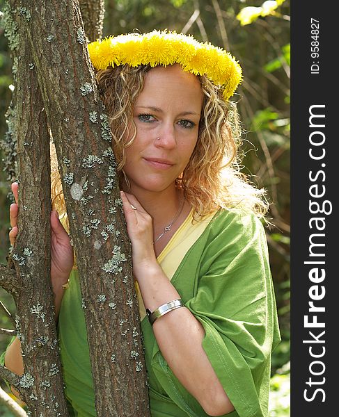 Curly girl with dandelion chain on head standing behind thin tree