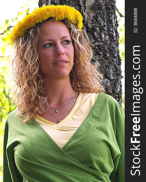 Curly girl with dandelion chain on head standing in front of birch tree