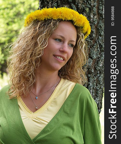 Curly girl with dandelion chain on head standing in front of birch tree