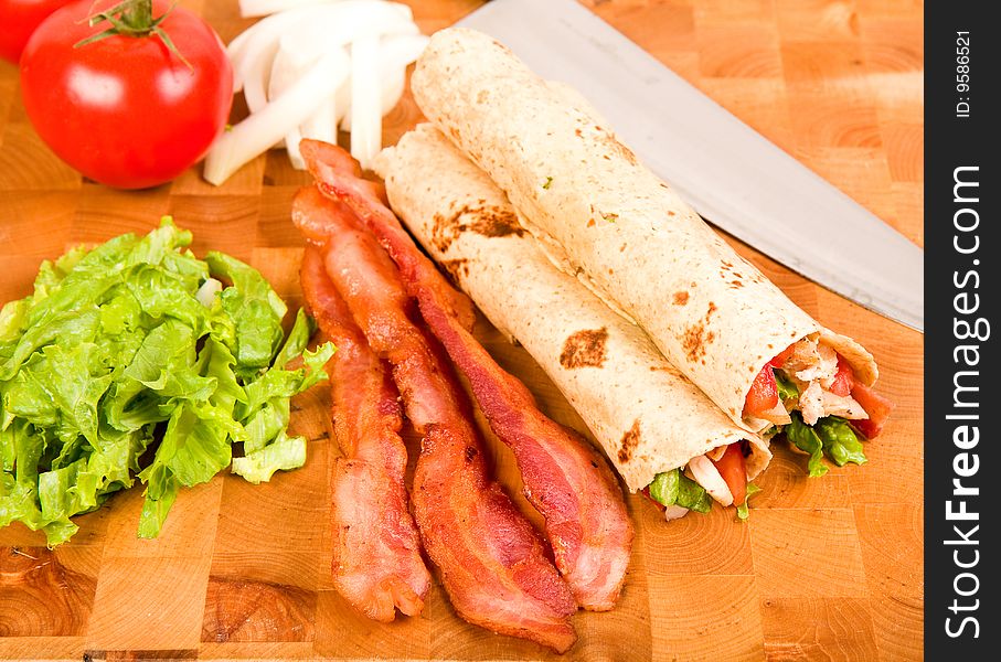 Chicken tortilla wraps on cutting board with tomato, bacon, onion and lettuce