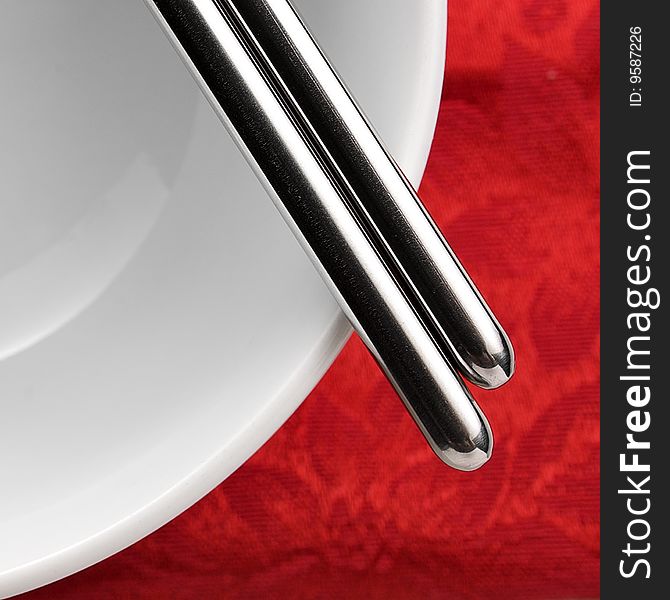 Close up shot of chopsticks on a white bowl over red table cloth