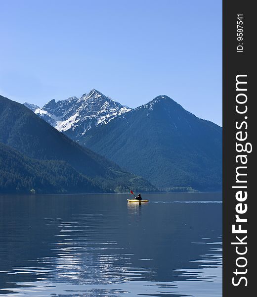 A lone kayaker paddles on Chilliwack Lake with rugged peaks in the background. A lone kayaker paddles on Chilliwack Lake with rugged peaks in the background.