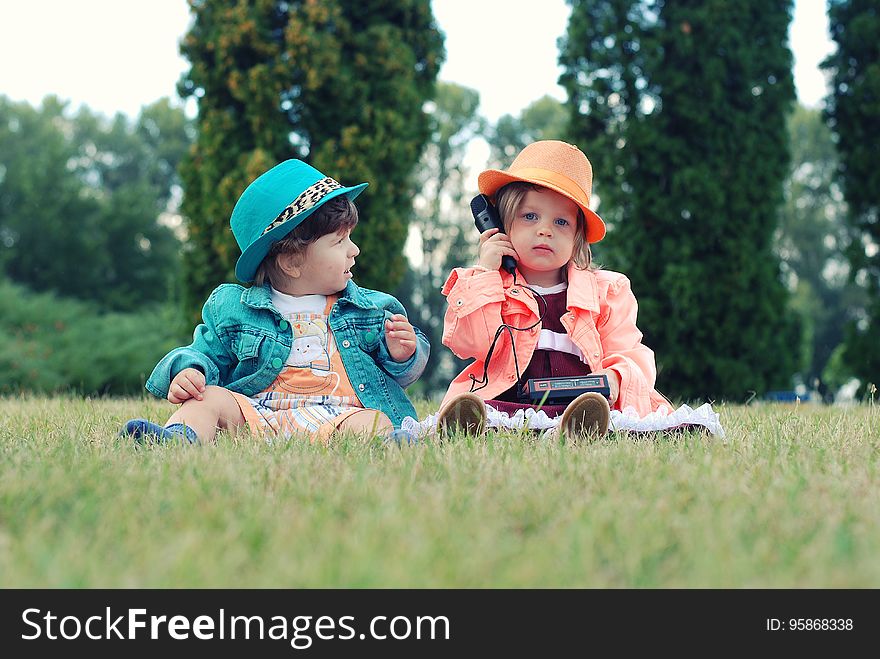 Portrait of children wearing coats and hats sitting in green grass outdoors playing with toy phone. Portrait of children wearing coats and hats sitting in green grass outdoors playing with toy phone.