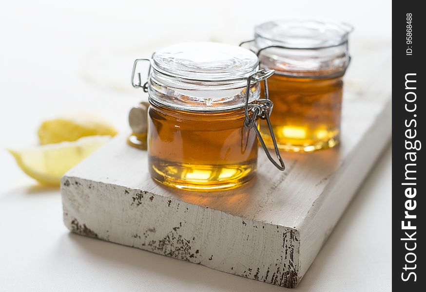 Close up of jars of honey on rustic wooden board with lemon wedges.