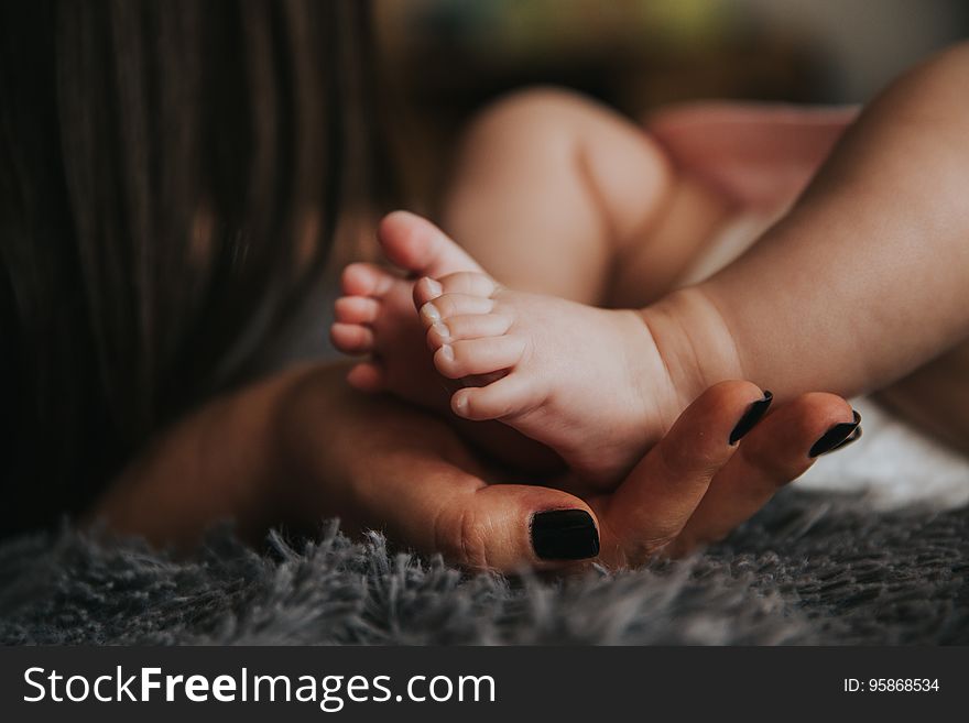 Close up of woman's hands holding feet of newborn baby on carpet. Close up of woman's hands holding feet of newborn baby on carpet.