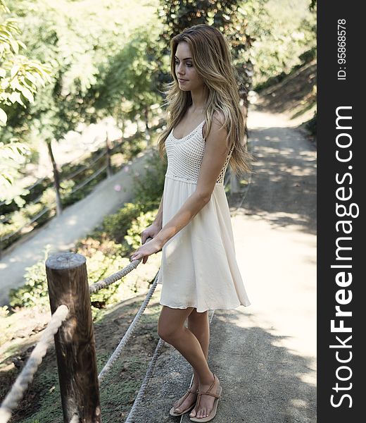 A pretty young woman in a white dress standing on a path by a fence. A pretty young woman in a white dress standing on a path by a fence.