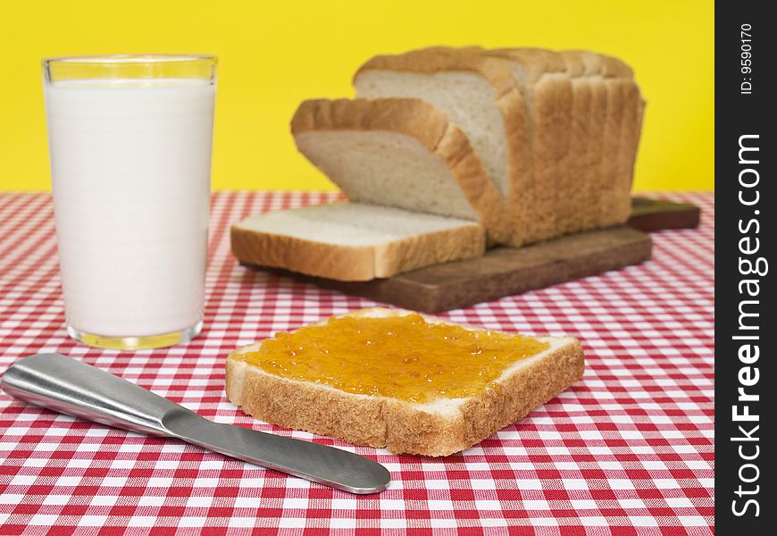 A slice of bread spread with jam beside a loaf of bread and a glass of milk. A slice of bread spread with jam beside a loaf of bread and a glass of milk.