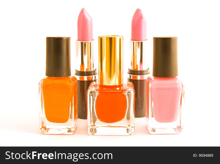 Three bottles of red, pink and orange nail polish with two pink lipsticks on a white background. Three bottles of red, pink and orange nail polish with two pink lipsticks on a white background