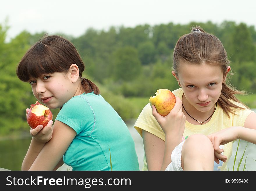 Two young girls eating apples on nature background. Two young girls eating apples on nature background