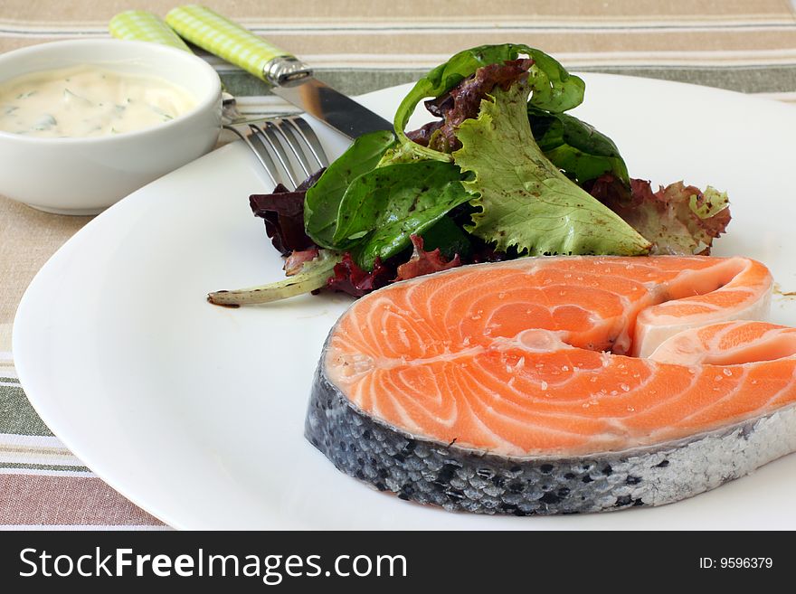 Fresh salmon steak on white platter with salad
