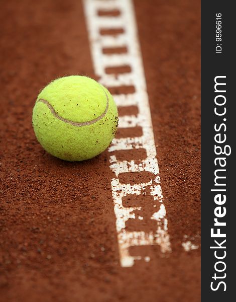 A tennis ball sits barely touching the line on a tennis court. A tennis ball sits barely touching the line on a tennis court