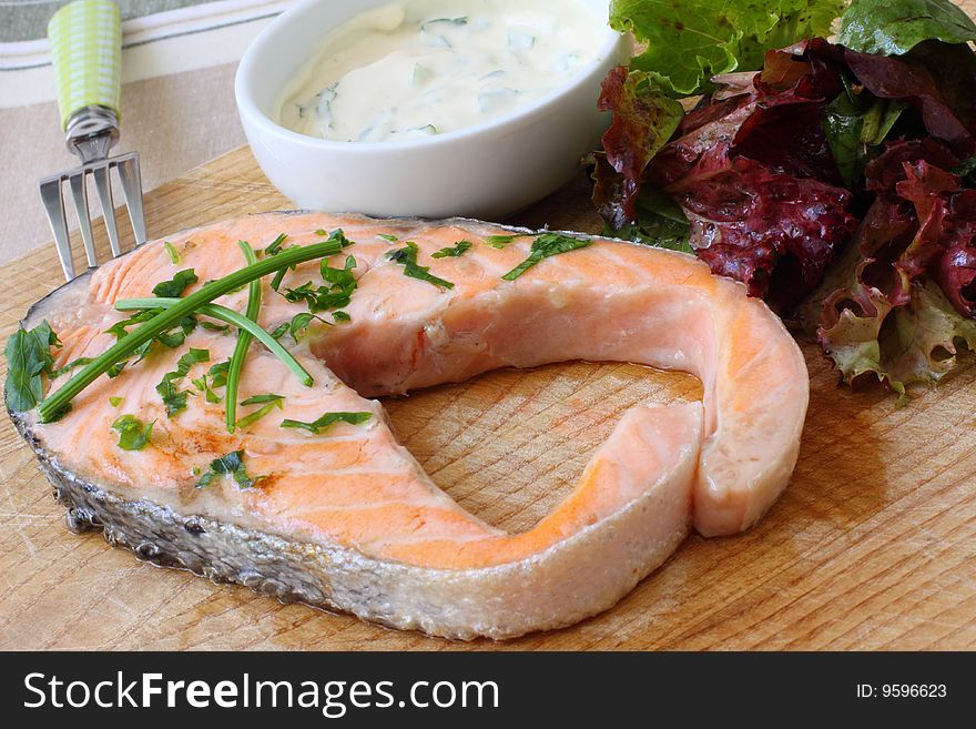 Grilled salmon steak on wooden board with salad