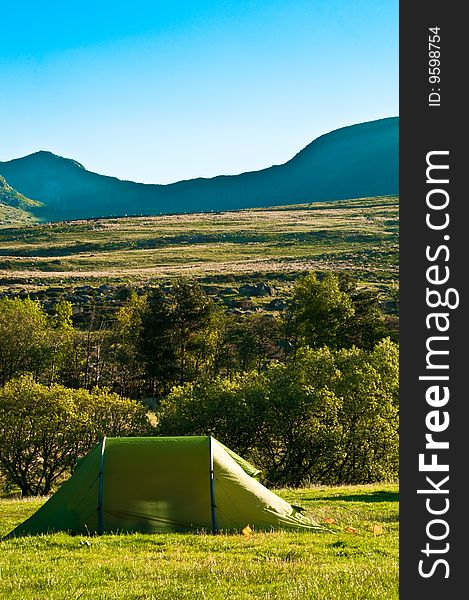 Single green tent in a field with mountains. Single green tent in a field with mountains