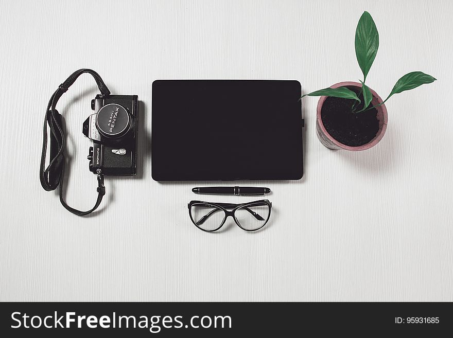 Still life with camera, tablet, eyeglasses, pen and potted plant on desktop. Still life with camera, tablet, eyeglasses, pen and potted plant on desktop.