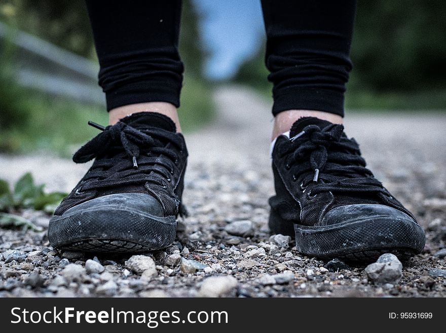 Close up of feet wearing black sneakers standing on rocks outside. Close up of feet wearing black sneakers standing on rocks outside.