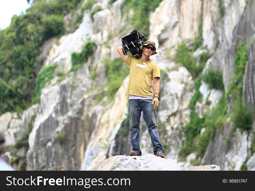 Cameraman with equipment standing on rocky ledge on sunny day. Cameraman with equipment standing on rocky ledge on sunny day.