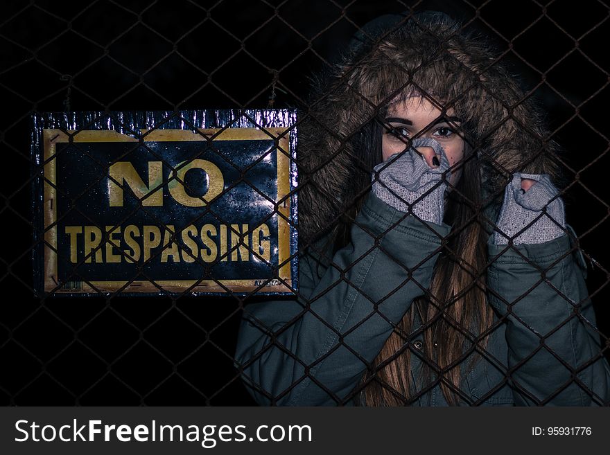 Young woman looking through fence at night next to no trespassing sign. Young woman looking through fence at night next to no trespassing sign.