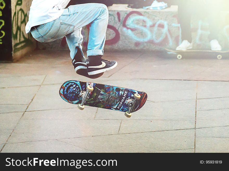 Feet and legs of skateboarder doing tricks in urban graffiti tagged skate park on sunny day.
