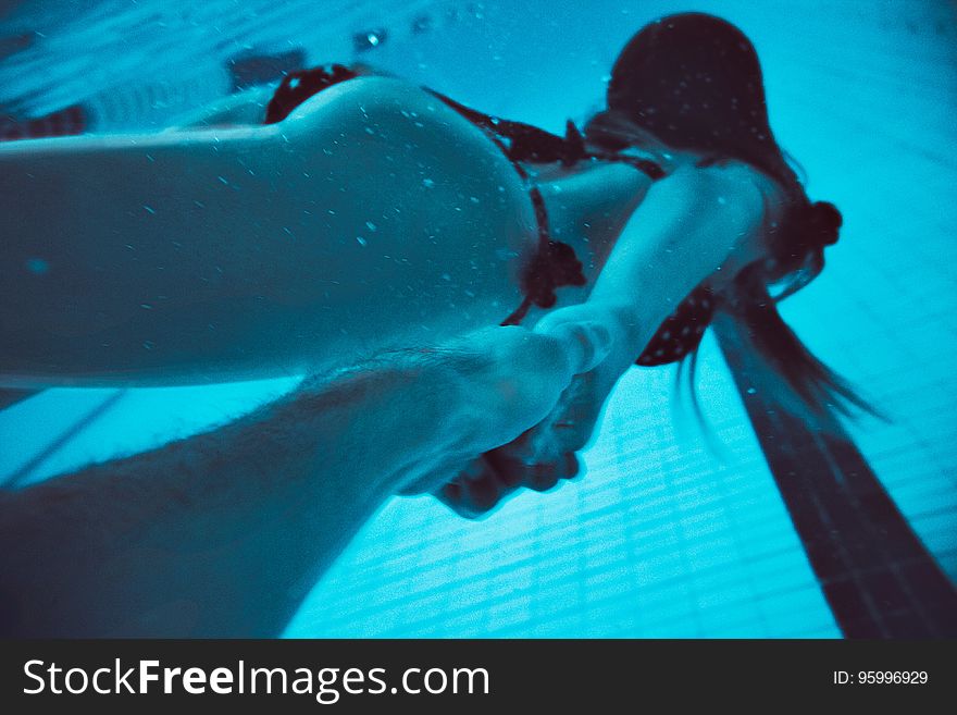Woman swimming underwater holding hands with someone.