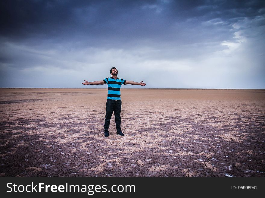 Man in black and blue striped shirt and pants standing in desert with open arms against clouds in blue sky. Man in black and blue striped shirt and pants standing in desert with open arms against clouds in blue sky.