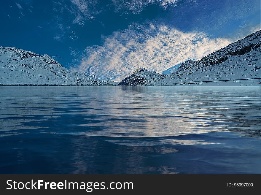 Clouds reflecting in blue waters of alpine lake with snow covered peaks on sunny day. Clouds reflecting in blue waters of alpine lake with snow covered peaks on sunny day.