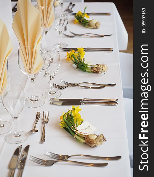 Table set for formal dinner with linens, silverware and glasses with bouquet of daffodils and name tags. Table set for formal dinner with linens, silverware and glasses with bouquet of daffodils and name tags.