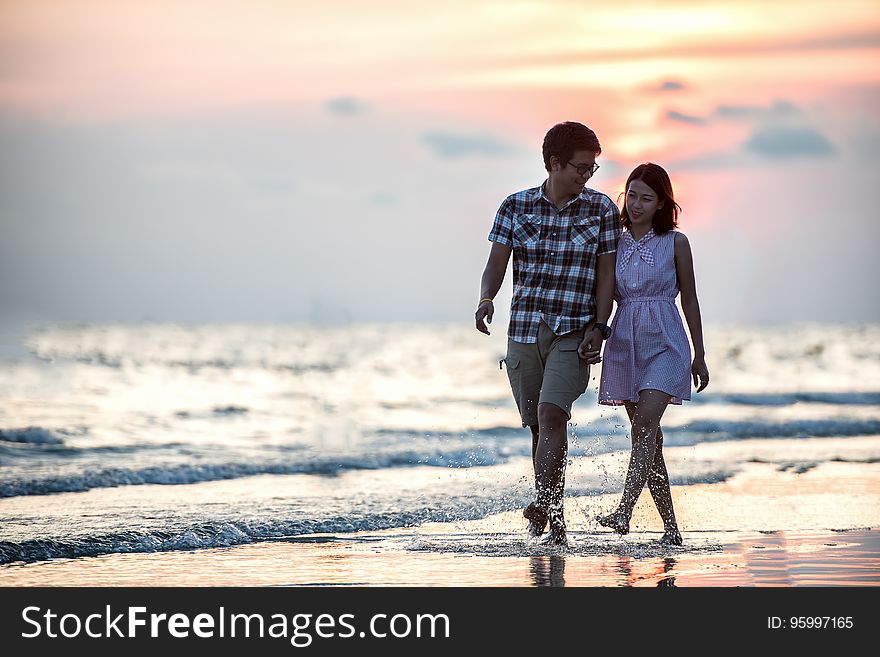 Couple holding hands strolling on beach at sunset. Couple holding hands strolling on beach at sunset.