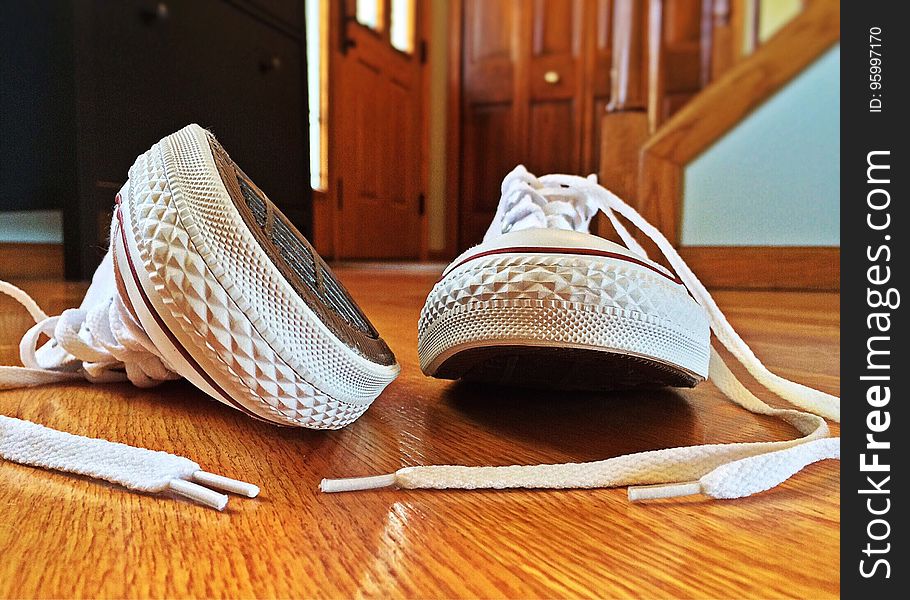 Close up of Converse white sneakers on wooden floor inside house.