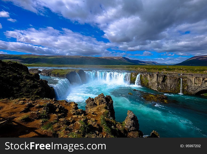 Scenic view of cascading waterfall down steep cliffs on wide river with cloudscape background. Scenic view of cascading waterfall down steep cliffs on wide river with cloudscape background.