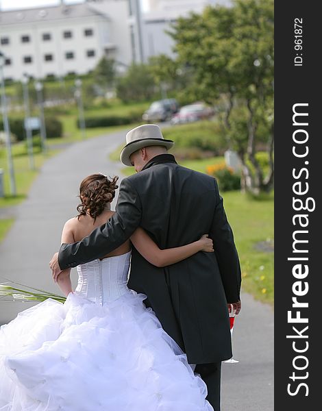 Young newlywed couple holding eachother as they walk away from camera. Young newlywed couple holding eachother as they walk away from camera